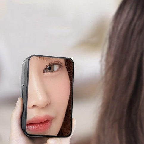 Close-up of a person holding a compact mirror reflecting their face, highlighting detail and skin tone