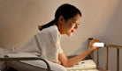 A young woman using a magnetic charging lamp for dormitory, featuring stepless dimming, while relaxing in bed