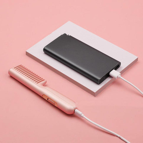 Portable USB charging negative ion hair comb in pink beside a black power bank for easy styling and smoothing