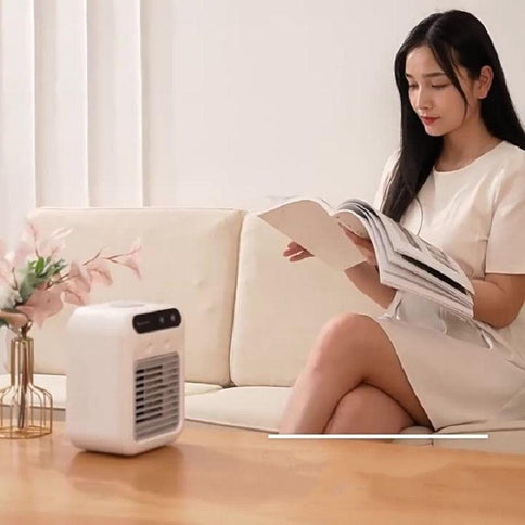 A woman sitting on a couch with a portable water cooling fan for office use on a table, enjoying a book in a well-lit room