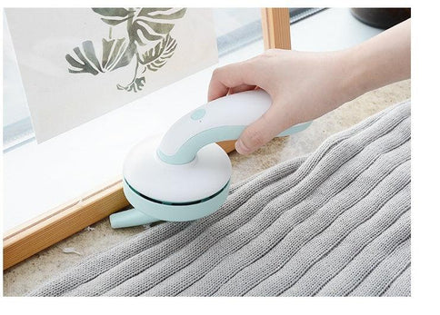 A hand using a USB desktop vacuum for home to clean a windowsill, featuring a sleek design in light colors