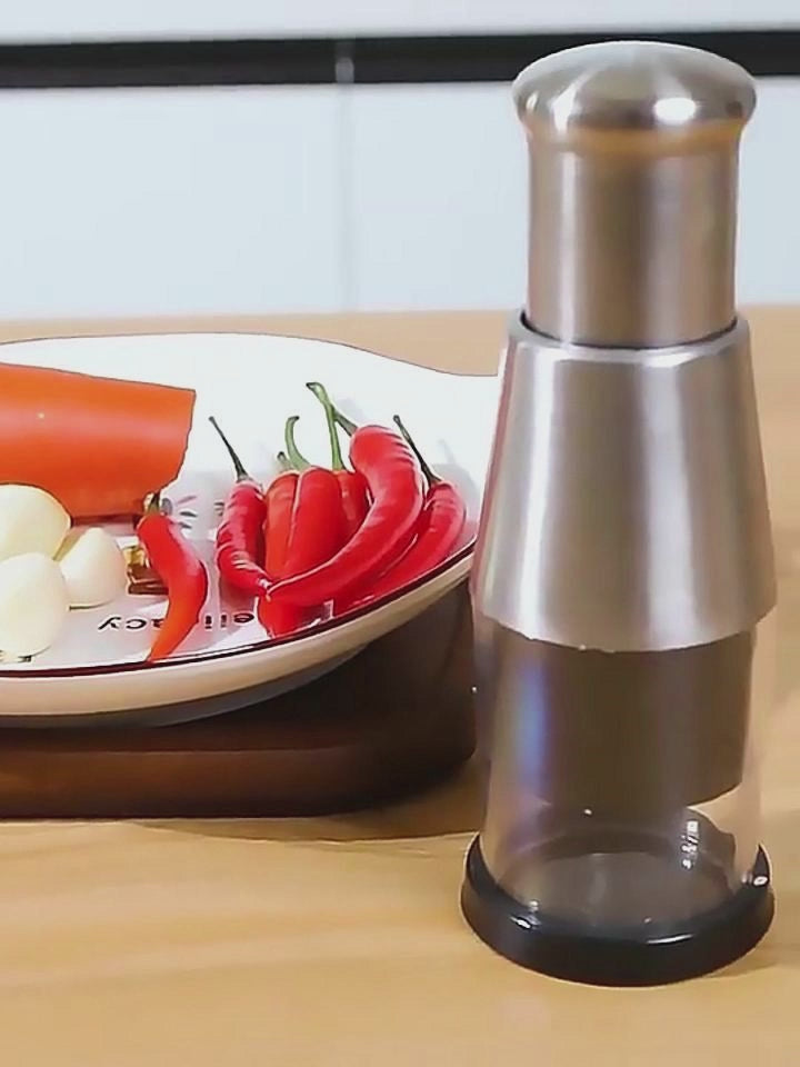 Stainless steel vegetable chopper and garlic press beside fresh red chili and vegetables on a plate, perfect for meal prep.